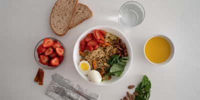 A balanced meal featuring a variety of healthy ingredients including noodles, eggs, almonds, strawberries, and fresh vegetables.