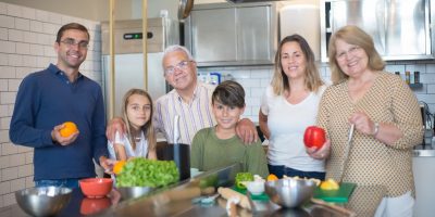A family of six smiling while preparing food in a modern kitchen.