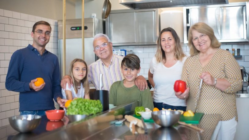 A family of six smiling while preparing food in a modern kitchen.