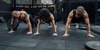 Three individuals performing push-ups together in a Mexico City gym setting.