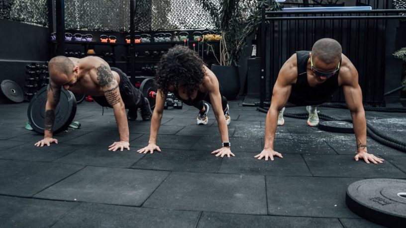 Three individuals performing push-ups together in a Mexico City gym setting.